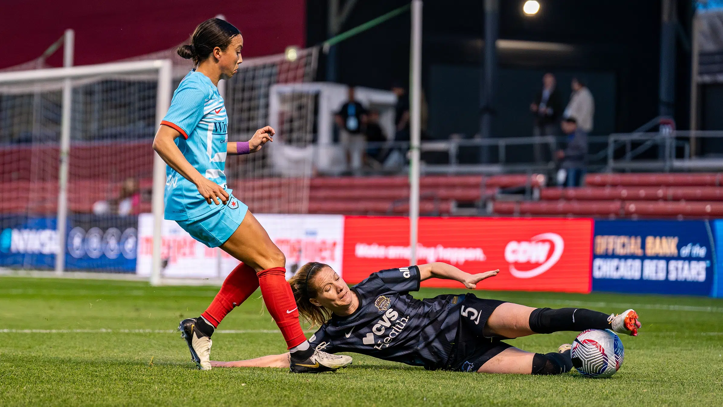 Annaig Butel in a black Spirit kit slide tackles the ball away from Mallory Swanson in a bright blue kit.