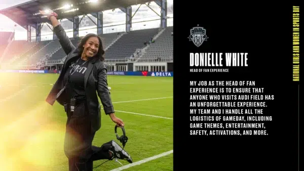 Donielle White in black pants, a black shirt, and a black blazer, standing and smiling on the pitch at Audi Field.