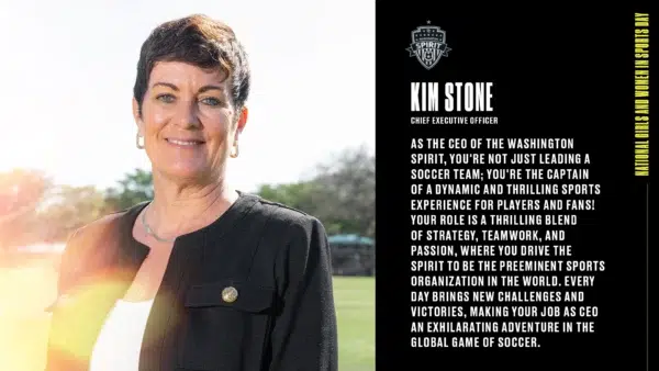 A headshot of Kim Stone smiling with a black jacket over a white top. In the background is a soccer field and trees.
