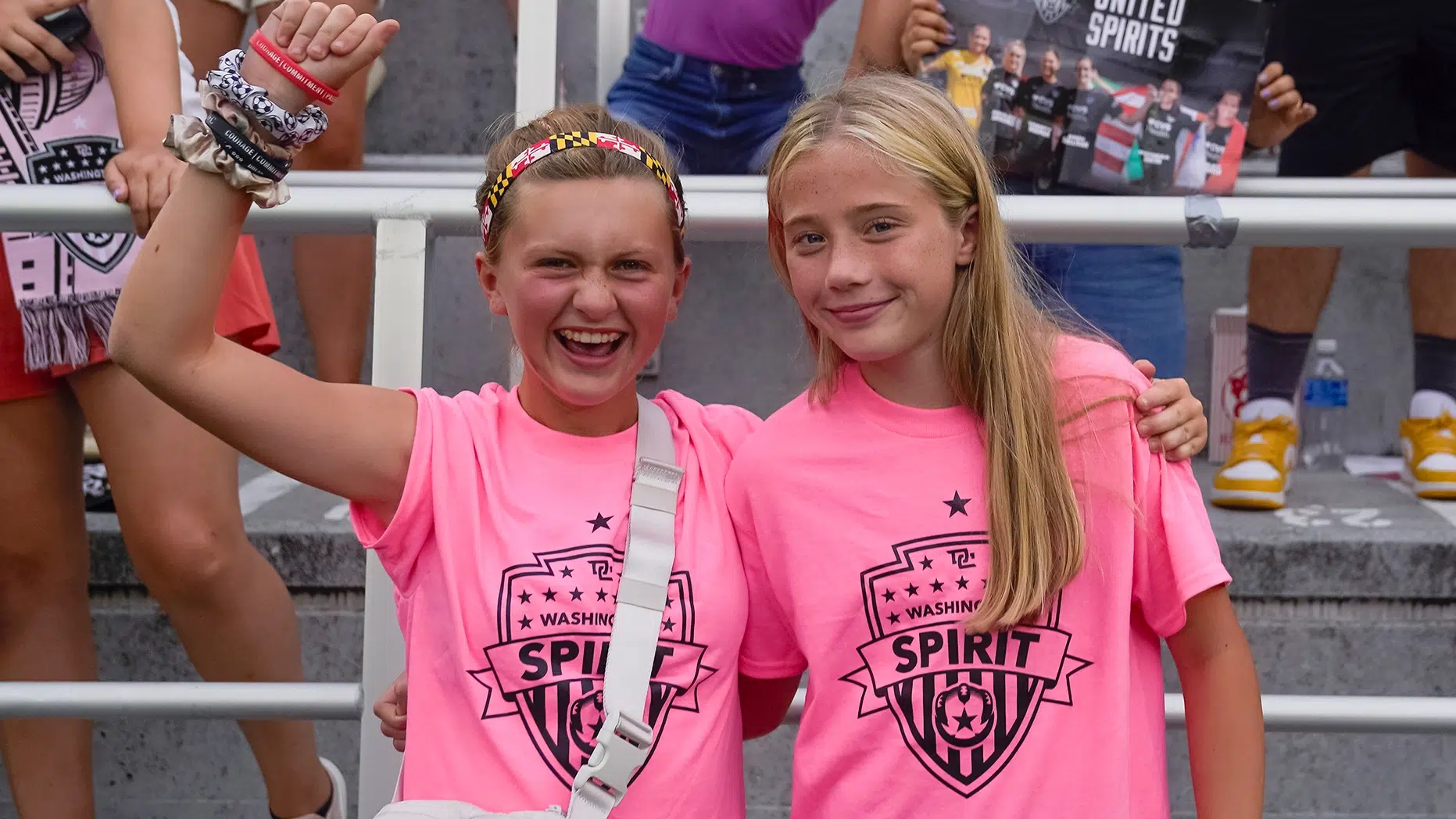 Two young girls cheer while wearing a pink t-shirt with a black Spirit crest.