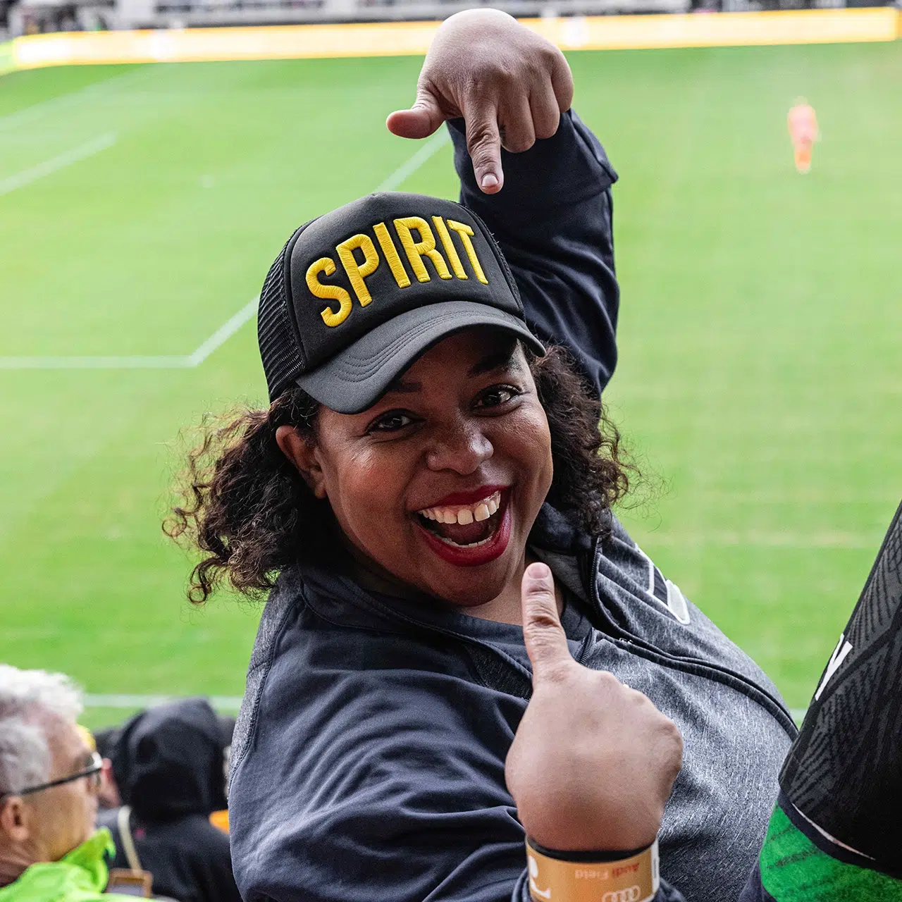A fan points to her black and yellow SPIRIT hat.