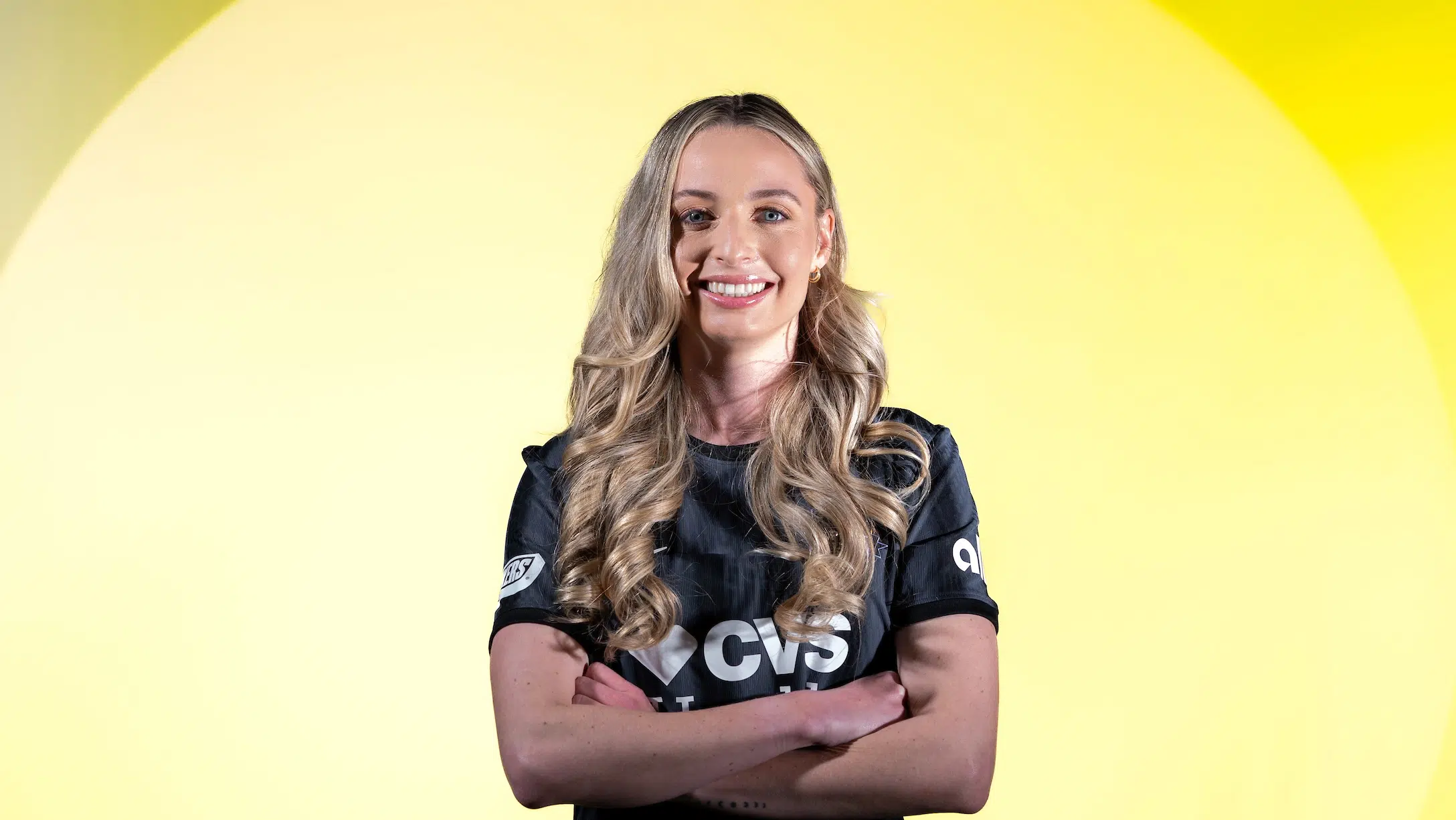 Gabby Carle in a black Spirit jersey with her arms crossed in front of a yellow background.