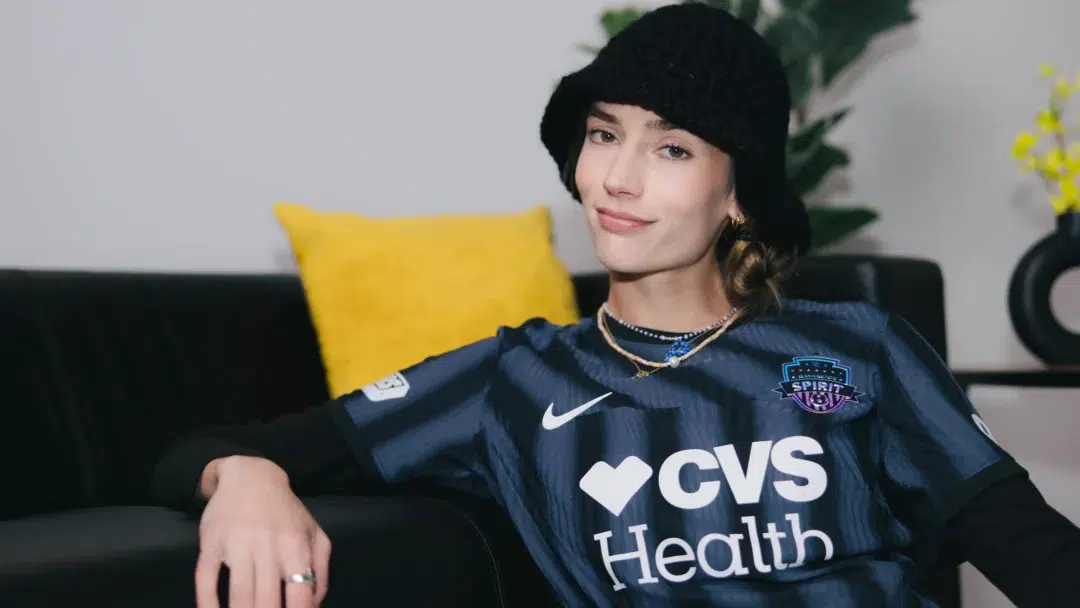 Paige Metayer lounges on a couch while wearing a black jersey and a black bucket hat.