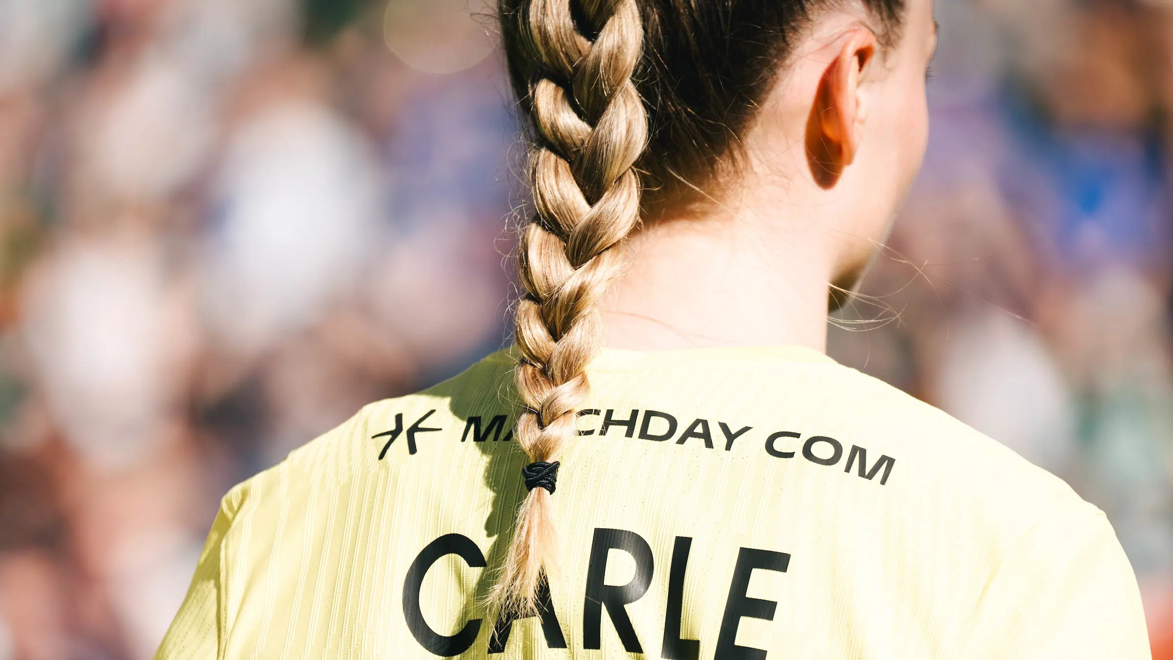 The back of Gabby Carle in a yellow Spirit jersey with her last name CARLE across the back. Her blonde braid falls over the name.