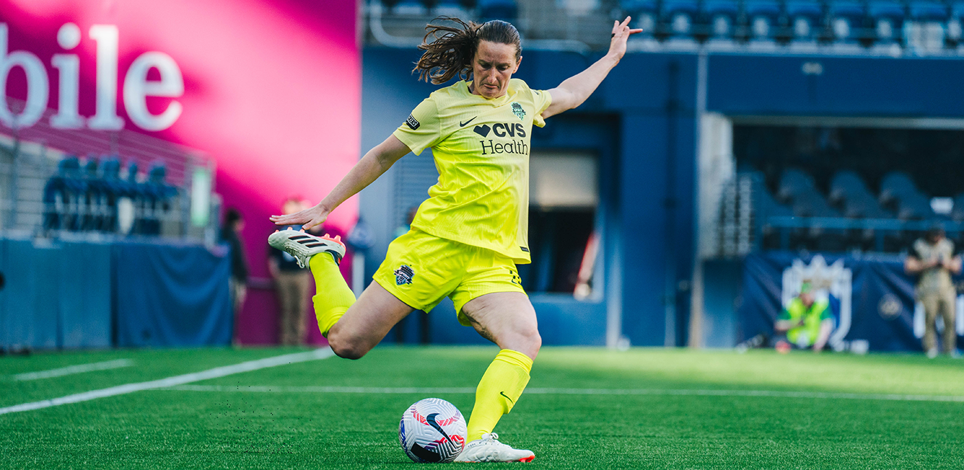 Andi Sullivan in a yellow Spirit kit winds up to kick a soccer ball with her right foot.