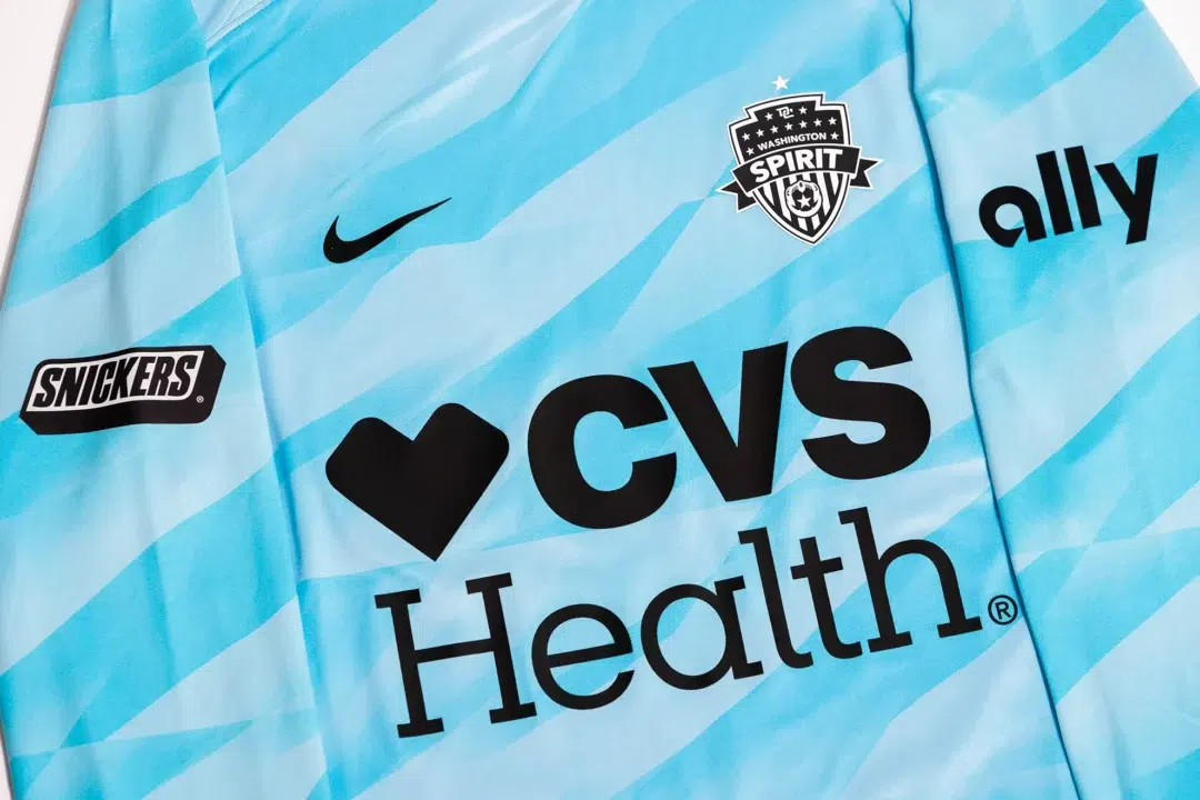 A blue, long-sleeved goalie jersey for the Washington Spirit. The front of the shirt has the Spirit crest, Nike Swoosh, and CVS Health logo. On the sleeve, a Snickers logo and the other sleeve has an Ally logo.