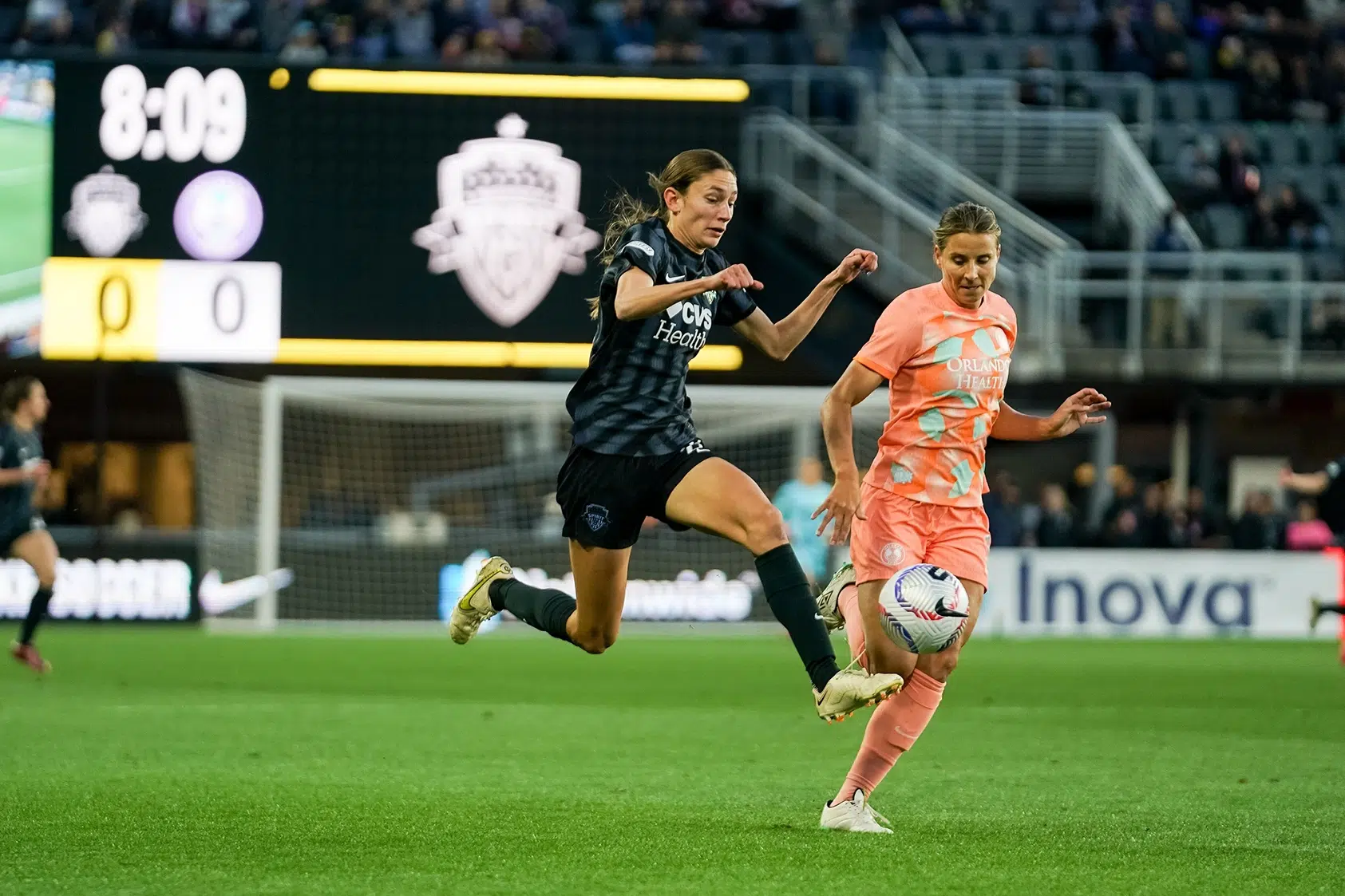 Paige Metayer controls a ball from the air while in a black kit. An Orlando defender in an orange kit closes in.