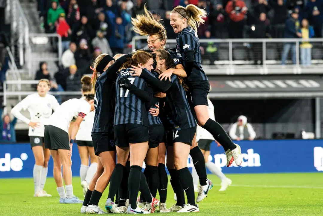 Spirit players in black kits jump and hug in celebration of a goal.