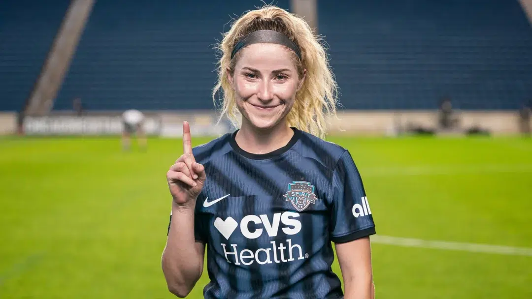 Heather Stainbrook holds up one finger while wearing a black Spirit kit with her blonde curly hair in a ponytail.
