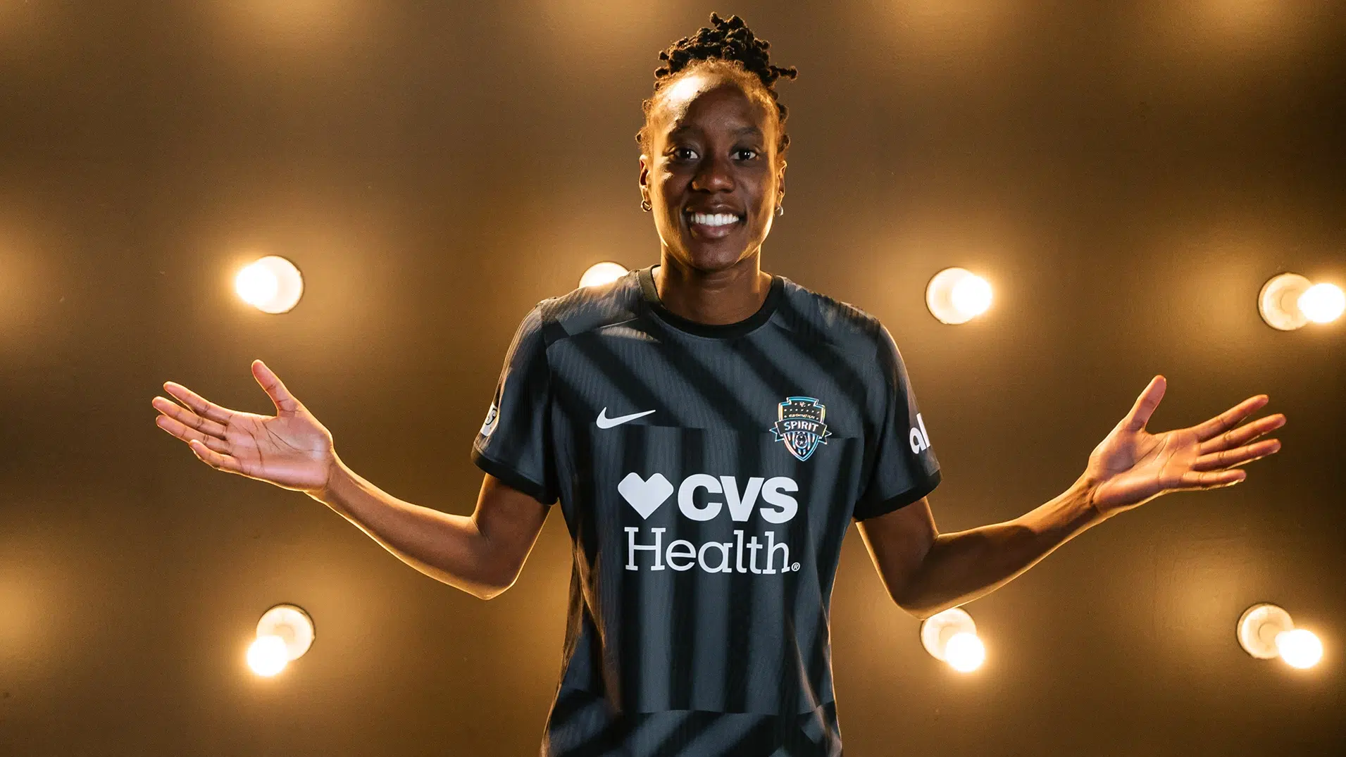 Ouleye Sarr in a black Spirit kit in front of a wall of light bulbs.