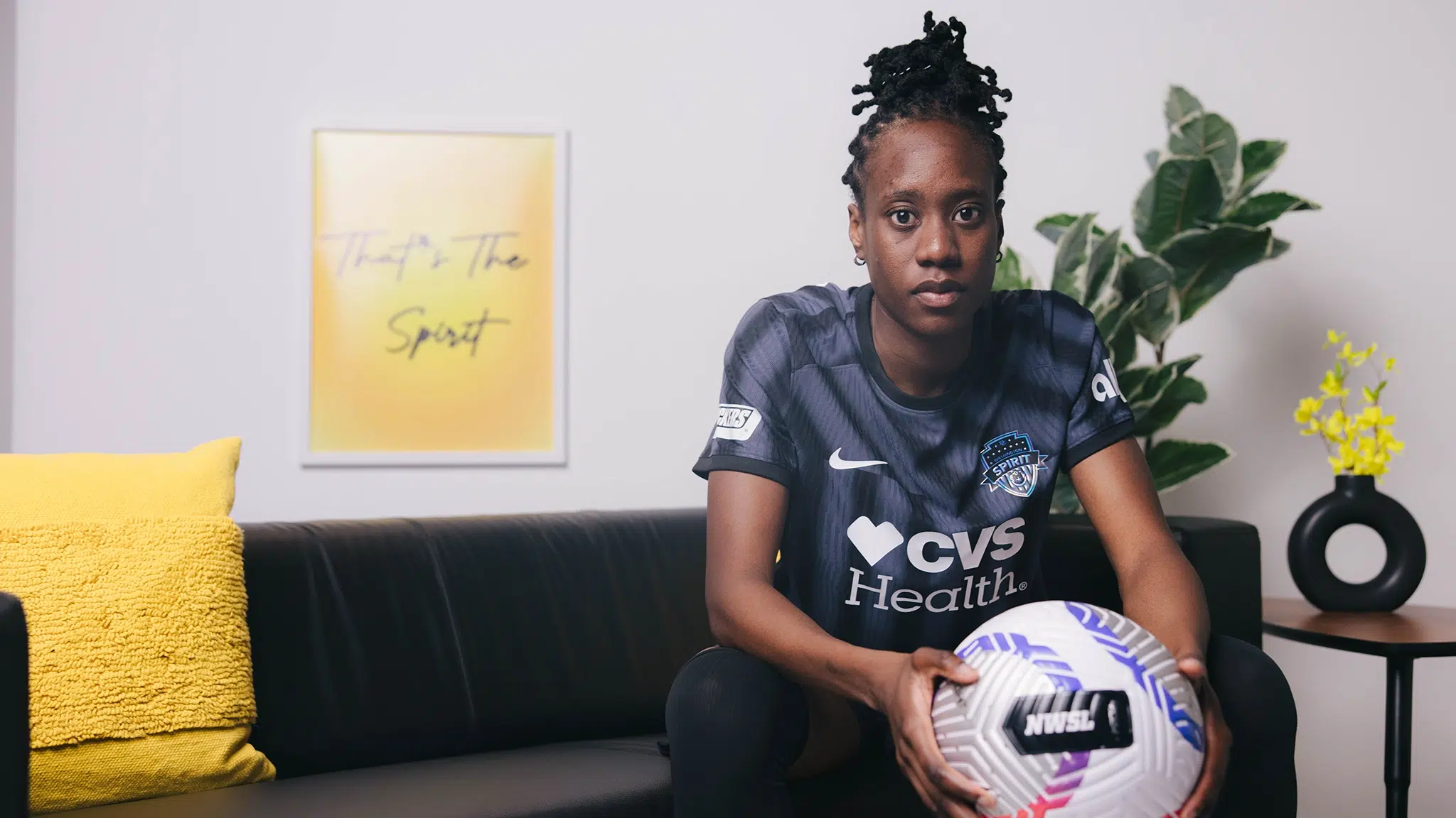 Ouelye Sarr in a black Spirit cake while sitting on a couch holding a soccer ball.