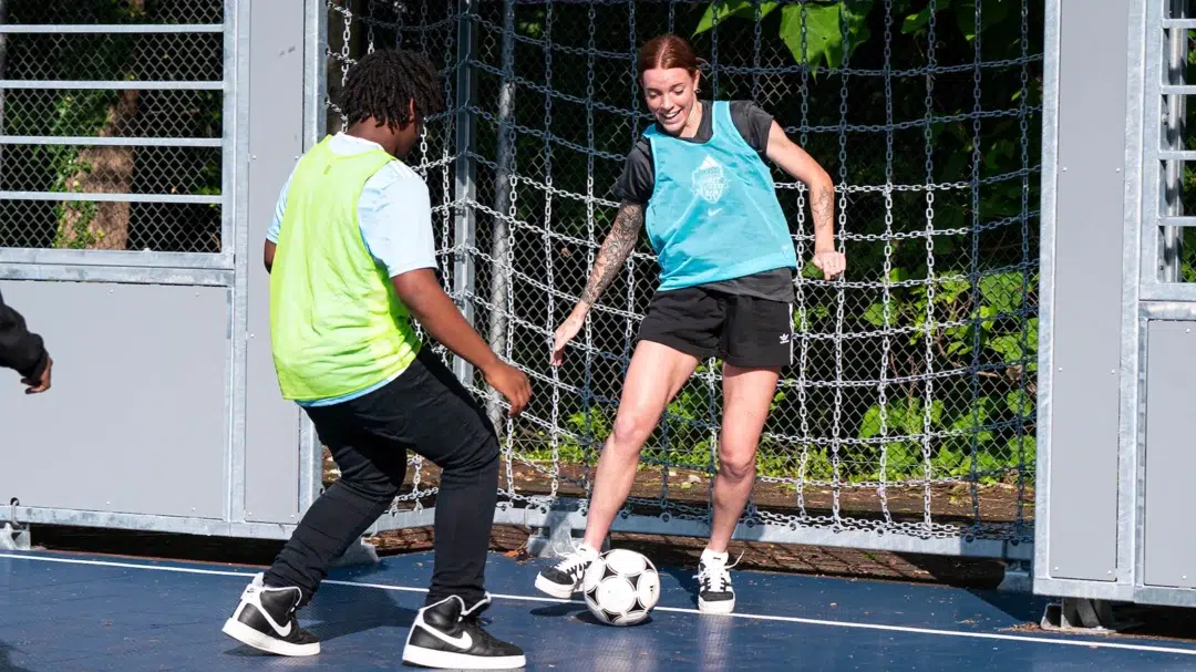 Hal Hershfelt dribbles a soccer ball towards a young boy.