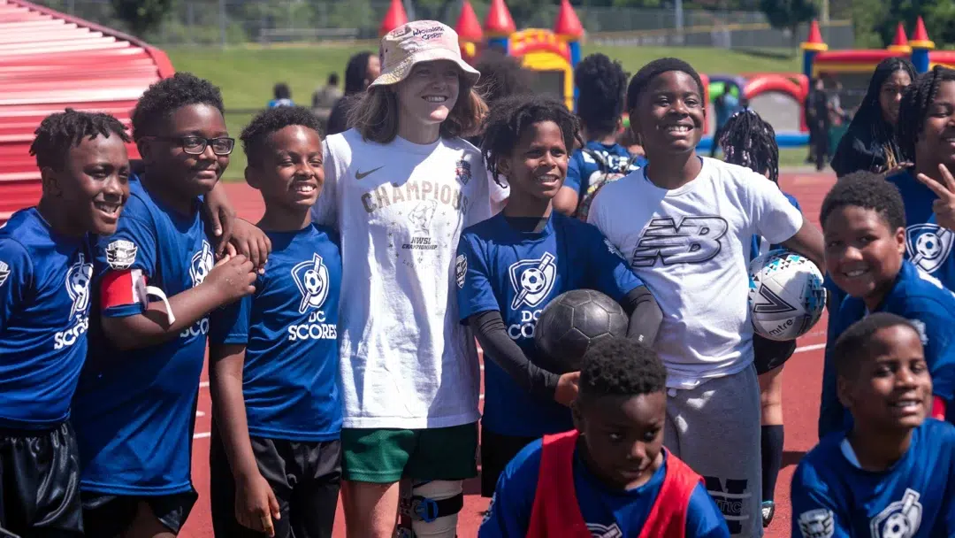 A group of young kids in blue soccer uniforms pose for a photo with Anna Heilferty.