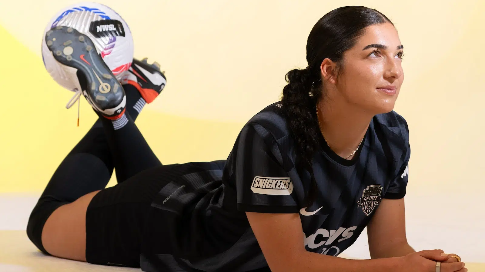 Lena Silano in a black kit lies down with a soccer ball balancing on her feet.