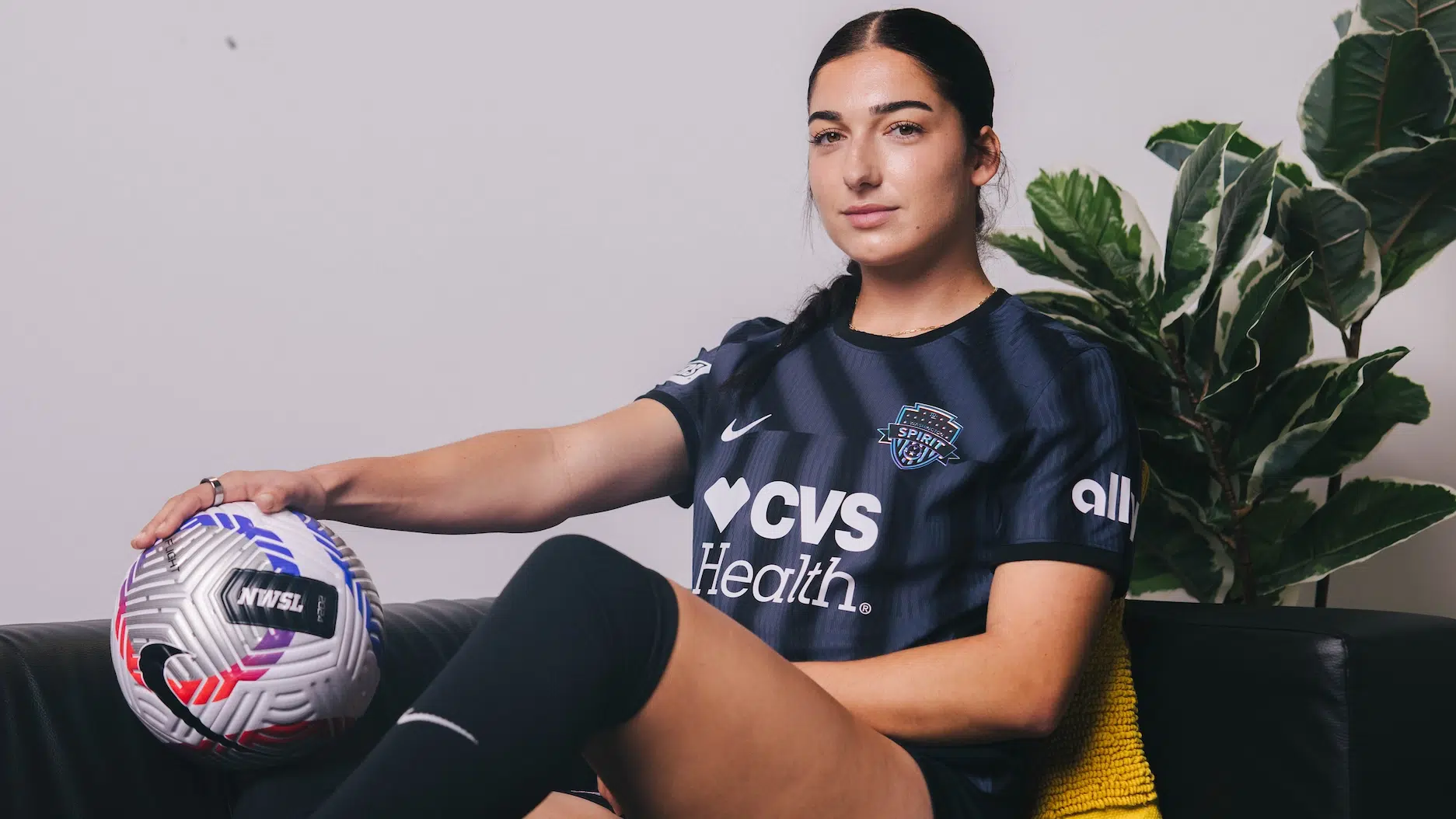 Lena Silano in a black kit sitting on a black couch.