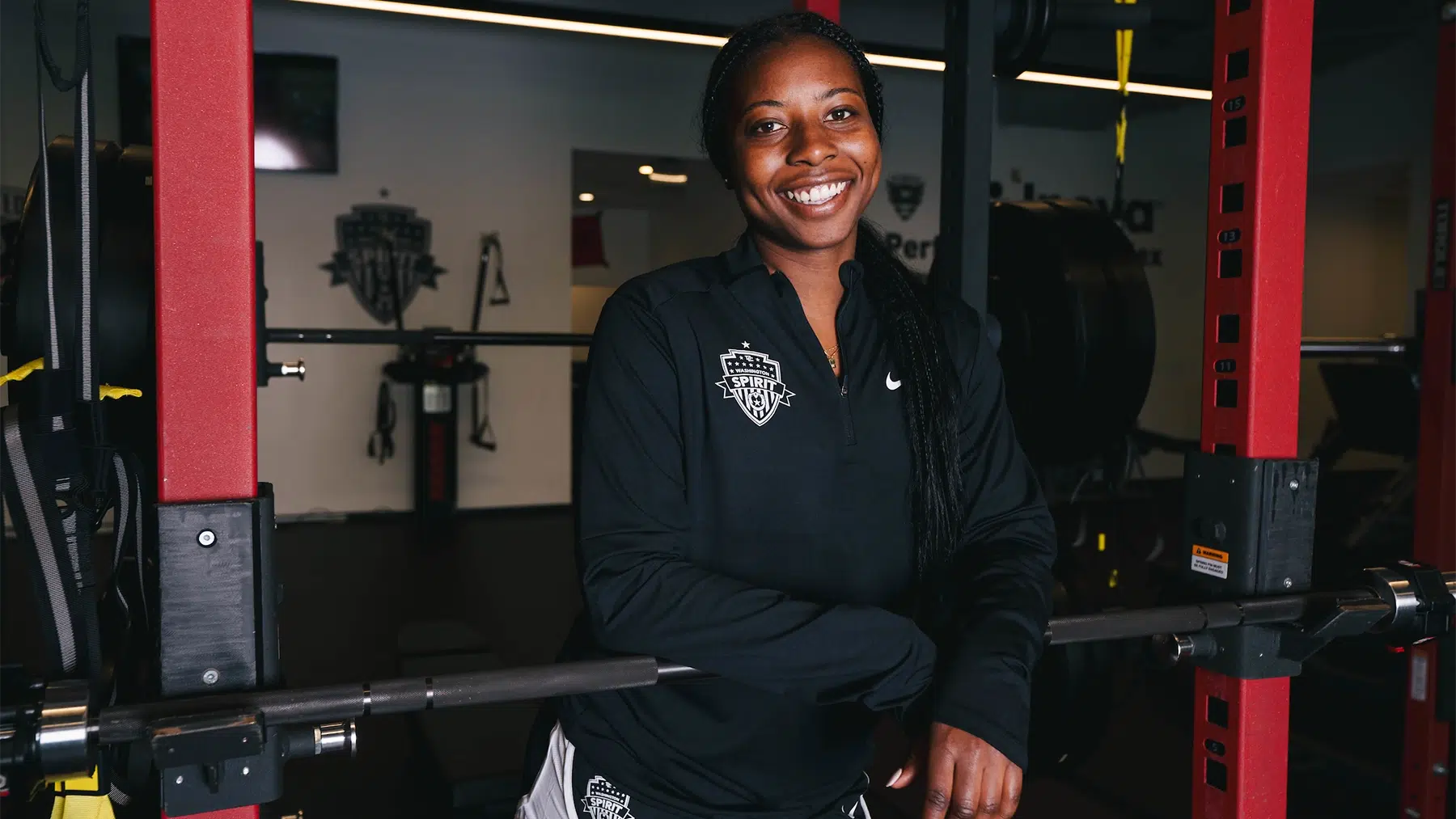 Waniya Hudson in a black quarter-zip in a weightlifting gym.