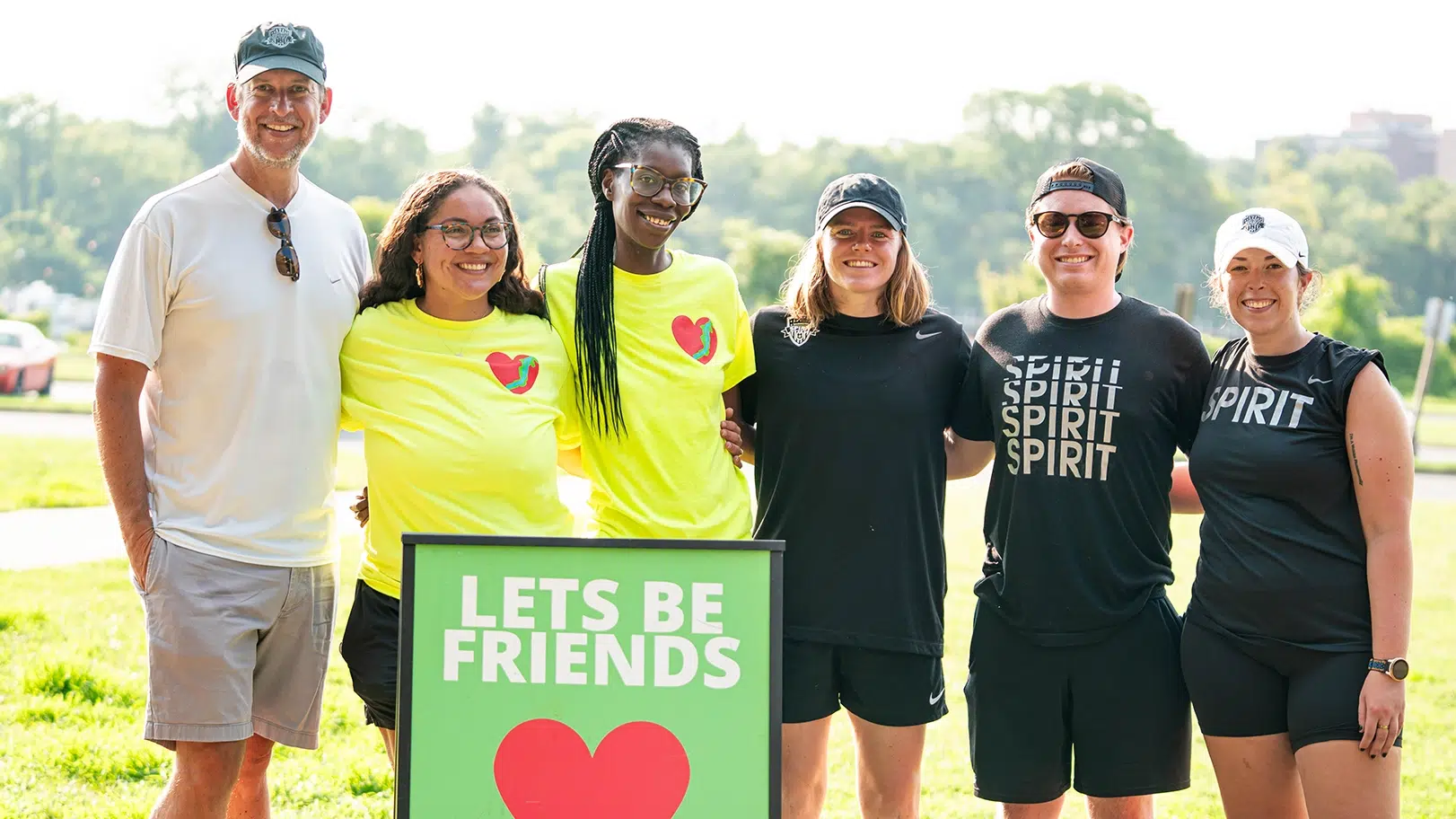 A group of smiling people. One in white, two in neon yellow, and three in black.