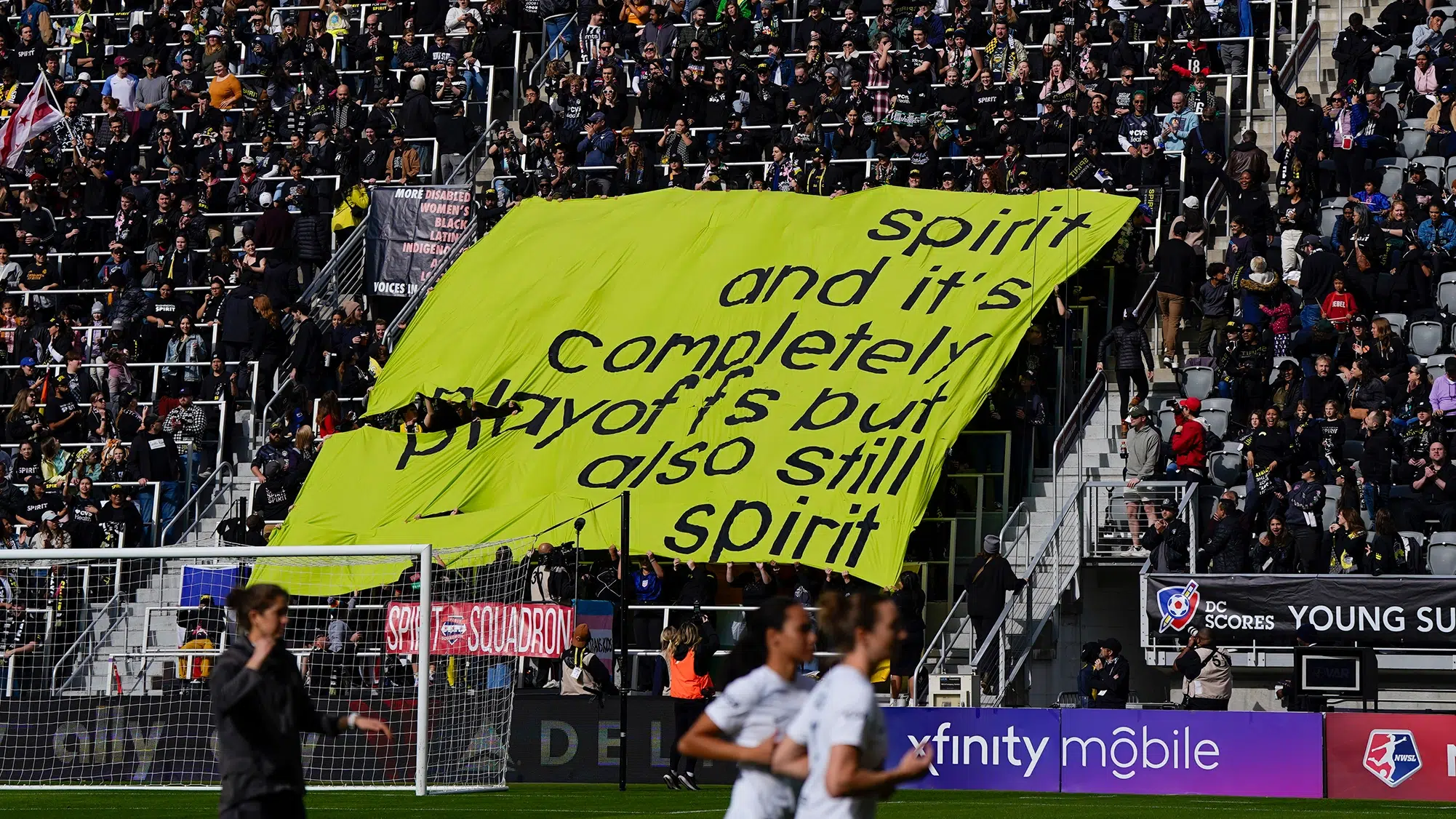 Spirit supporters hold up a lime green tifo reading "spirit and it's completely playoffs but also still spirit".