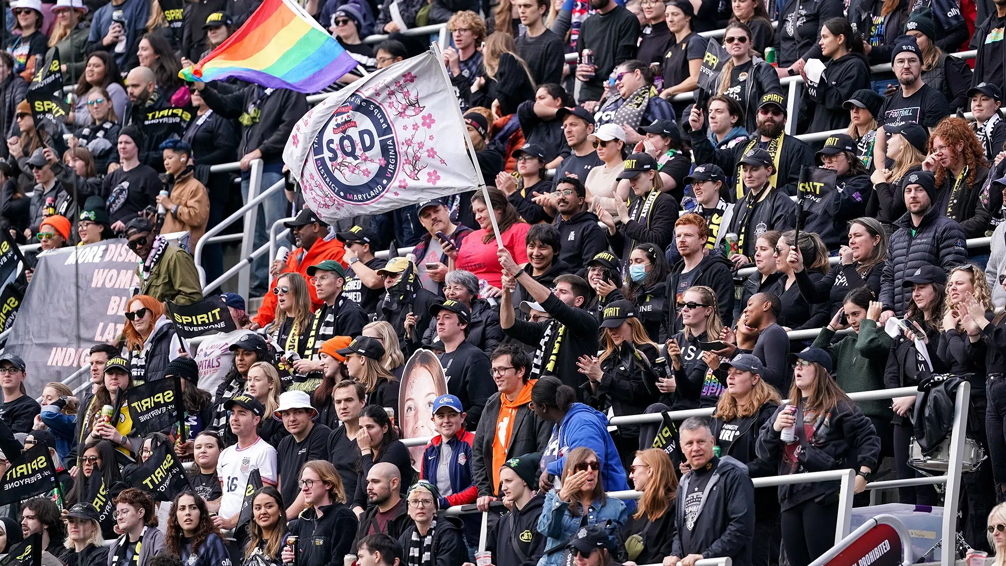 Spirit fans dressed in black waves flags and cheer.