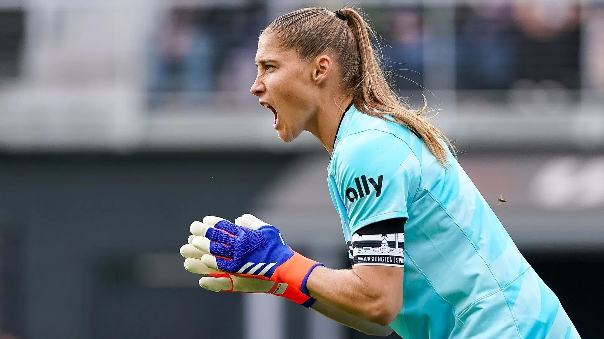 Aubrey Kingsbury in a blue goalkeeper jersey yells and claps her hands.