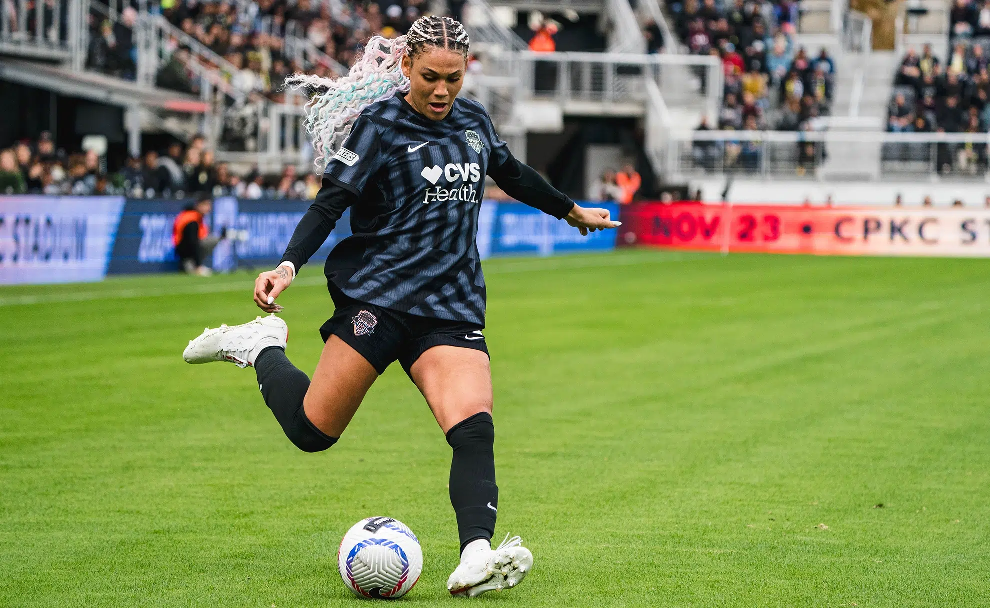 Trinituy Rodman with pale blue and pink braids prepares to kick the ball.