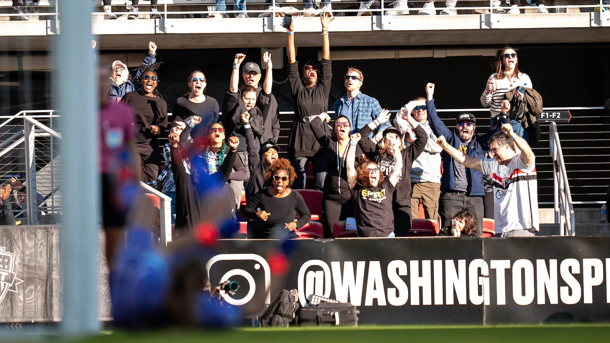 Fans in focus in the background yell and celebrate. An out-of-focus Kingsbury in the foreground blocks a shot.