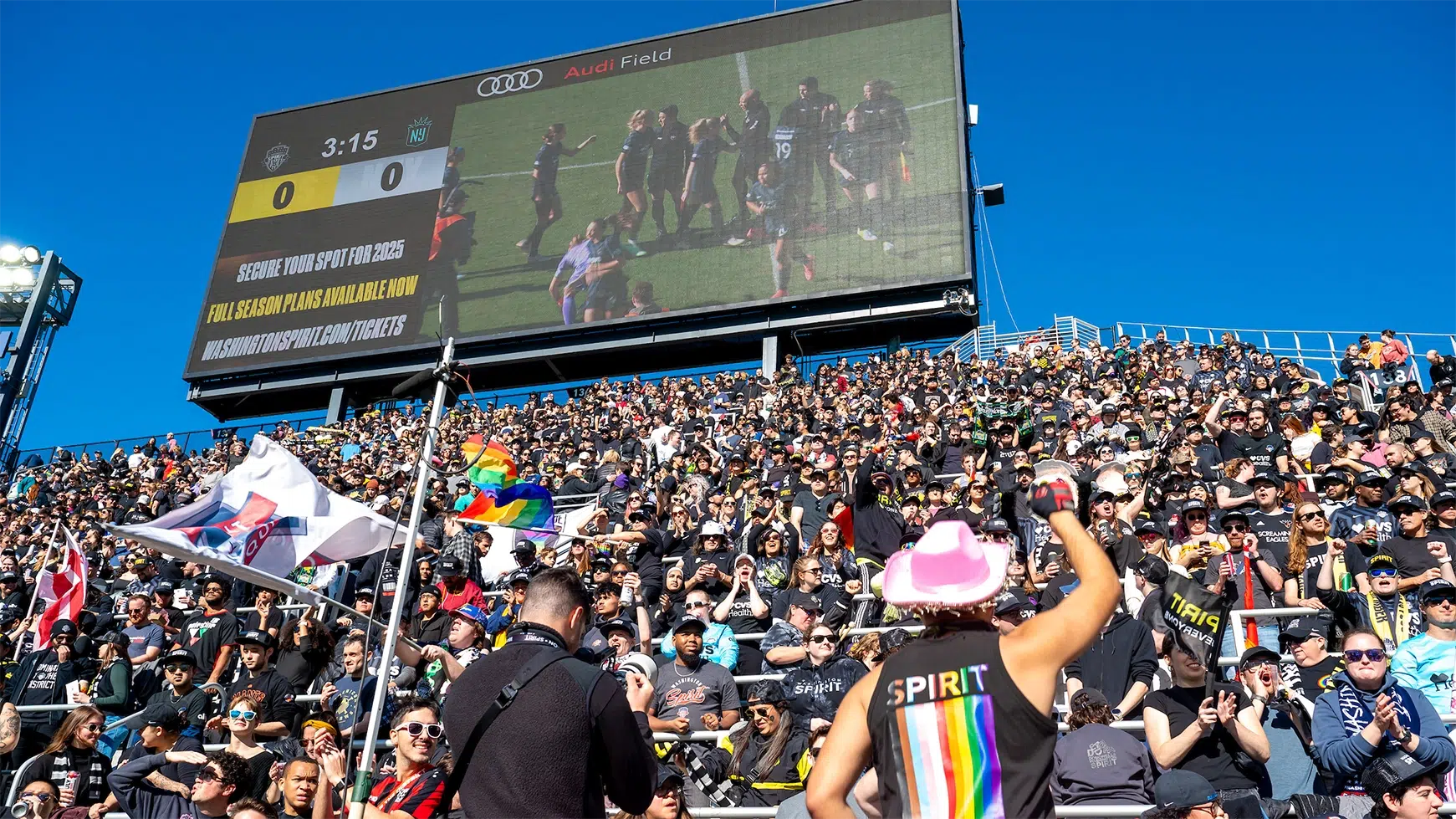 A crowd of standing fans in the supporters section of Audi Field.