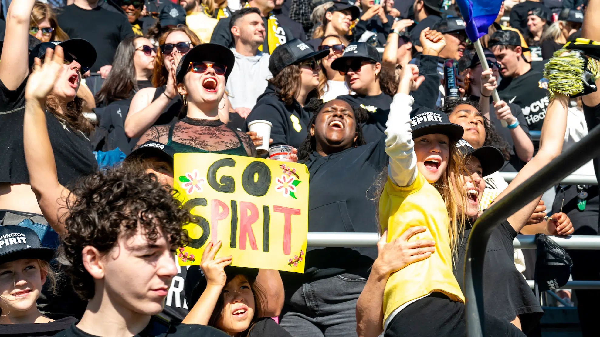 Spirit fans cheer. One fan dressed in black holds up a yellow poster that reads "Go Spirit"