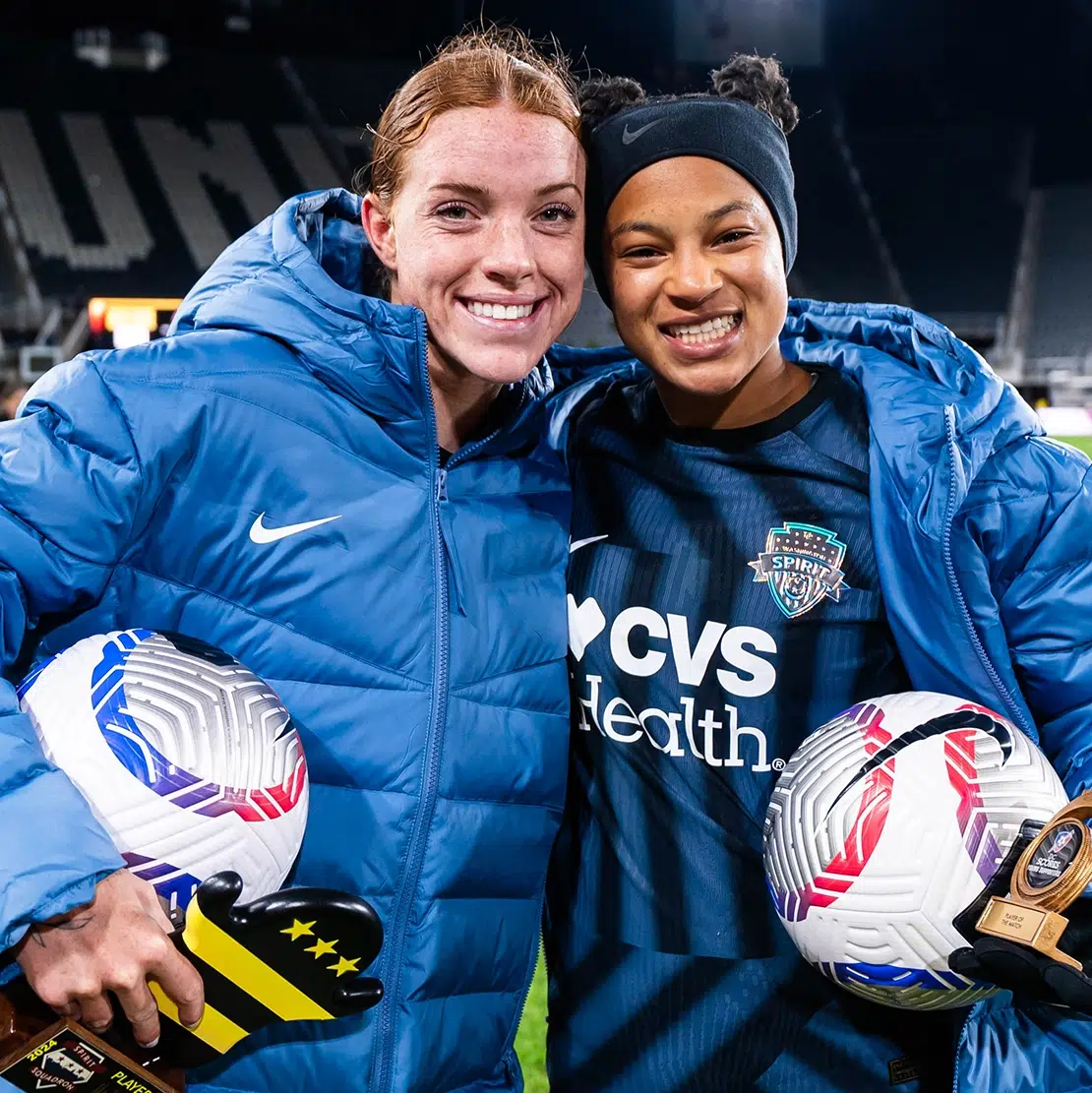 Hal Hershfelt and Croix Bethune in slate gray winter jackets holding soccer balls.