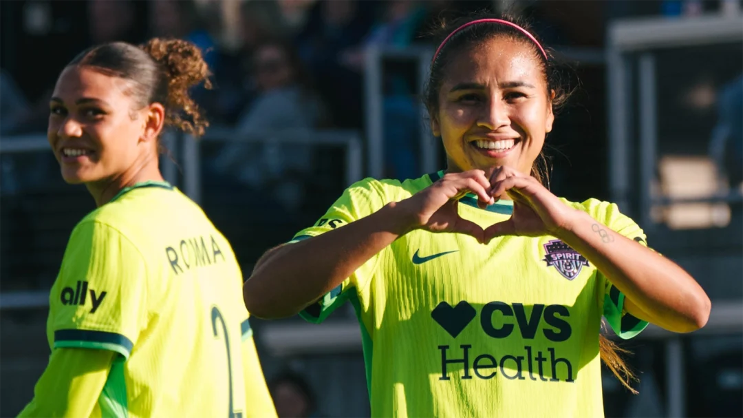 Leicy Santos makes a heart with her hands. Trinity Rodman smiles in the background.