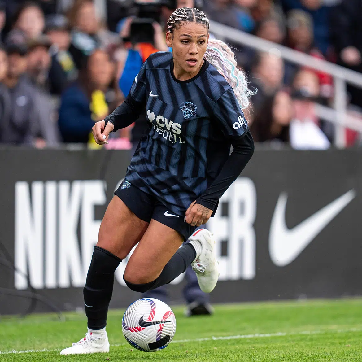 Trinity Rodman with pastel pink and blue braids dribbles a soccer ball.