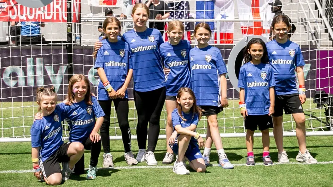 A group of young girls in matching blue soccer jerseys standing in front of a goal.