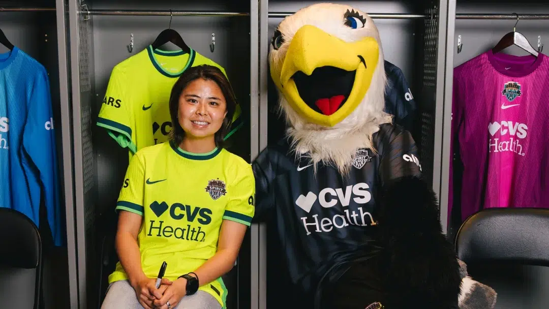 Narumi Miura sits next to PK--the Spirit's eagle mascot--in front of gray lockers.